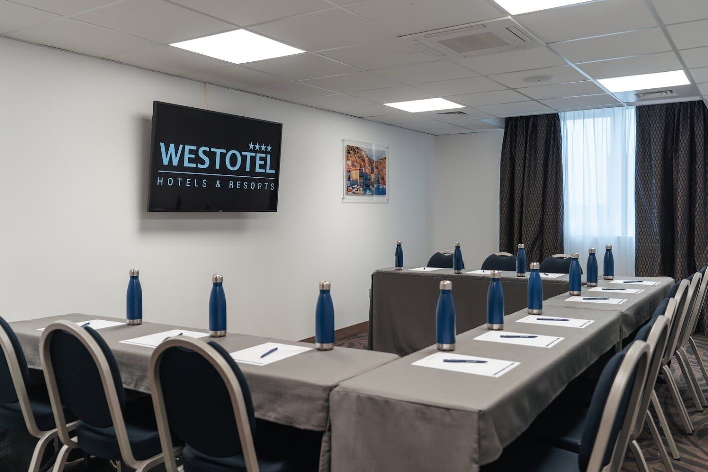 A conference room with a long table, chairs, water bottles, and a screen displaying "WESTOTEL HOTELS & RESORTS".