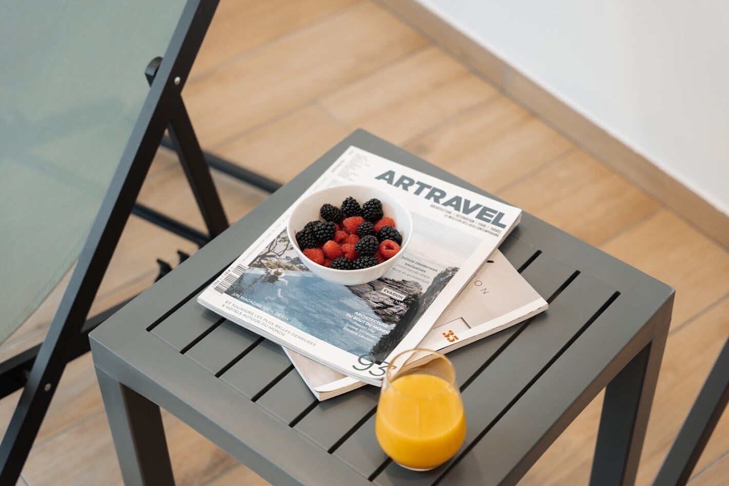 Una revista titulada 'ARTRAVEL' sobre una mesa pequeña, con un tazón de bayas y un vaso de jugo de naranja.