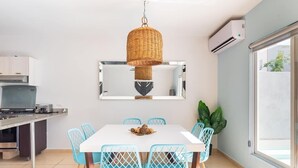 A modern kitchen with a white table and blue chairs, a hanging wicker chandelier, and an air conditioning unit. - House with Private Pool, Roof Garden, and BBQ Grill (Playa del Carmen)