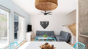 A modern living room with a white table, blue chairs, a grey sofa, a woven ceiling light fixture, and a wall-mounted TV. - House with Private Pool, Roof Garden, and BBQ Grill (Playa del Carmen)