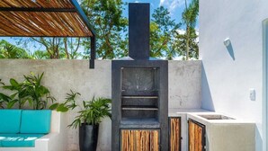 A modern outdoor kitchen with a built-in grill, seating area, and potted plants. - House with Private Pool, Roof Garden, and BBQ Grill (Playa del Carmen)