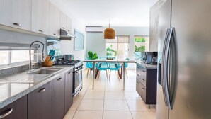 A modern kitchen with stainless steel appliances, a dining area with blue chairs, and a large window with plants. - House with Private Pool, Roof Garden, and BBQ Grill (Playa del Carmen)