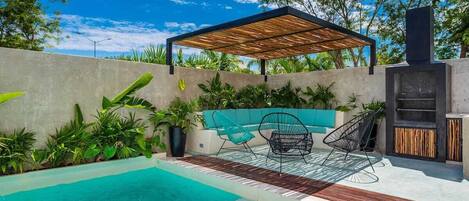 A swimming pool with a wooden deck, a covered seating area, and a barbecue grill.