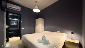 A modern hotel room with a large bed, a bedside table with a lamp, a wardrobe, and an air conditioning unit. - Cosy studio close to city center in Sants (L'Hospitalet de Llobregat)