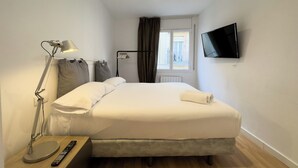 A hotel room with a bed, a desk with a lamp, a TV, and a window with curtains. - Comfortable 3-bedroom apartment with terrace, close to the center (L'Hospitalet de Llobregat)