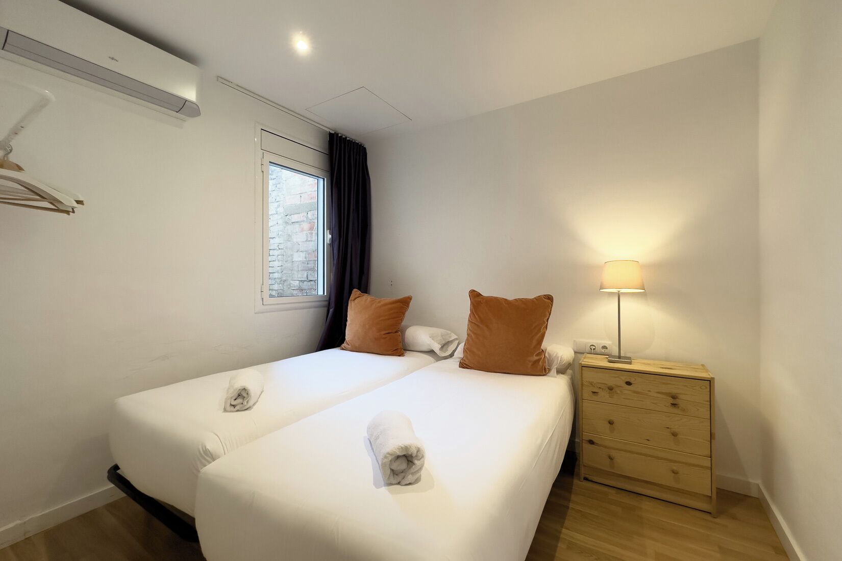 Une chambre d’hôtel avec deux lits, une fenêtre avec des rideaux, une lampe de chevet et une table de chevet en bois.