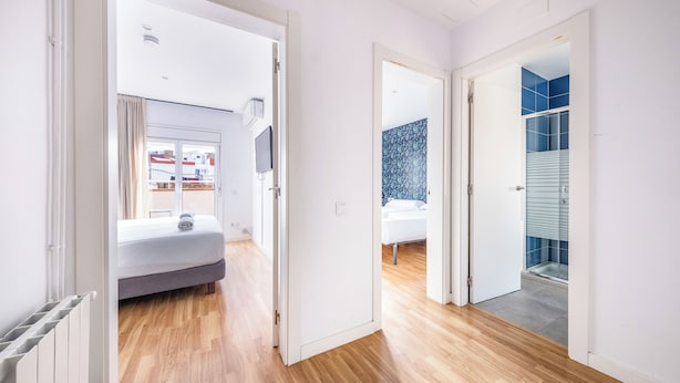 Habitación de hotel moderna con piso de madera, cama, baño con ducha de vidrio y vistas al exterior.