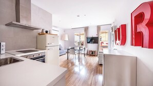 Una cocina moderna con estufa integrada, horno y una campana extractora grande. Hay un comedor con mesa y sillas, y un televisor montado en la pared.