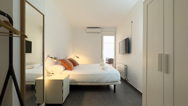 A modern hotel room with a bed, bedside table, mirror, and a TV mounted on the wall.