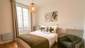 Et moderne hotelværelse med en stor seng, en grøn lænestol og to abstrakte malerier på væggen.