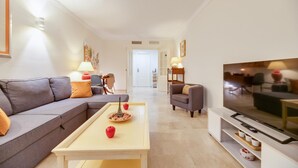 A modern living room with a grey sofa, a coffee table with decorative items, a TV, and a dining area in the background. - Urban Exclusivity At Puerto Banús (Marbella)