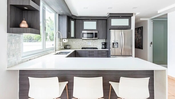 A modern kitchen with dark cabinetry, a large island with bar seating, a microwave, stove, and refrigerator. - Luxury Casa CALIAD (San Juan)