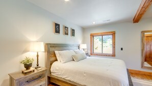 A bedroom with a wooden bed, a nightstand with a lamp, and a window with a view of greenery. - Secluded Livingston Retreat w/ Deck + Fire Pit! (Livingston)