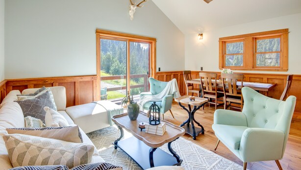 A spacious living room with a high ceiling, wooden beams, a large window with a view of trees, a dining area with wooden furniture, and a cozy seating arrangement. - Secluded Livingston Retreat w/ Deck + Fire Pit! (Livingston)