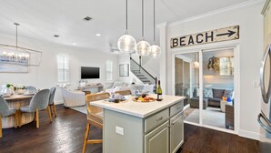 Une cuisine moderne avec un îlot central, un coin repas avec une table ronde et des chaises, et un panneau indiquant la direction de la plage.