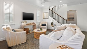 Un salon comprenant un canapé, des fauteuils, un téléviseur, un escalier et une cheminée.