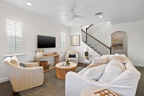 Ein Wohnzimmer mit einer Couch, Sesseln, einem Fernseher, einer Treppe und einem Kamin.