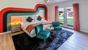 Une chambre à coucher moderne avec un grand lit, deux fauteuils verts, une petite table ronde et un tapis noir.