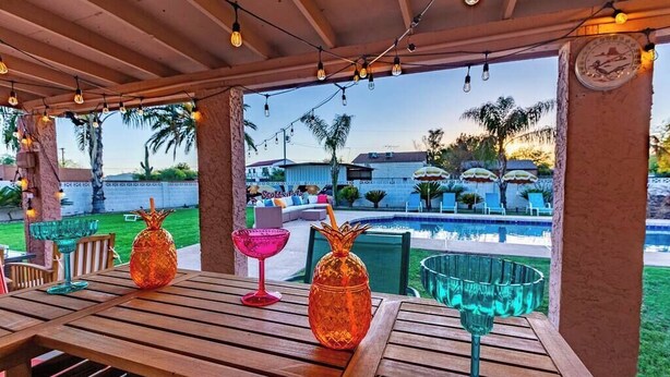 Une terrasse extérieure avec des tables en bois, des verres à cocktails et des guirlandes lumineuses.