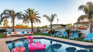 Une piscine avec des flamants gonflables, des chaises longues et des palmiers.