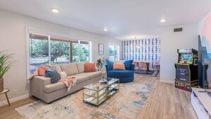Un salon spacieux comprenant un canapé, un fauteuil bleu, une table basse et une console de jeux.