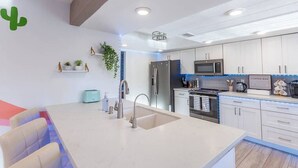 Une cuisine moderne avec des meubles blancs, un îlot central doté d’un évier, d’un réfrigérateur, d’un four à micro-ondes et d’un coin café.