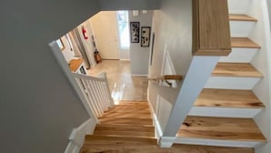 Eine Holztreppe mit weißen Geländern führt zu einem Raum mit einer Tür und einem Fenster.
