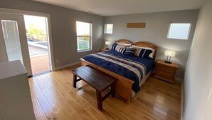 Ein Schlafzimmer mit einem Bett, Nachttischen, einer Bank und einer Glastür, die auf einen Balkon führt.