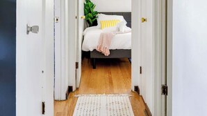 A hallway leading to a bedroom with a bed, a plant, and a framed picture on the wall. - Curated for Cozy Stays -2 Parking Spaces, Sleeps 4 (Westmont)