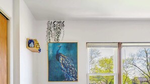 A dining area with a table set for two, a peacock painting on the wall, and a view of the outside through large windows. - Curated for Cozy Stays -2 Parking Spaces, Sleeps 4 (Westmont)