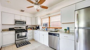 A modern kitchen with white cabinets, stainless steel appliances, a ceiling fan, and a window providing natural light. - Curated for Cozy Stays -2 Parking Spaces, Sleeps 4 (Westmont)