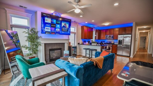 Un soggiorno moderno con un camino, una TV montata a parete e una cucina sullo sfondo.