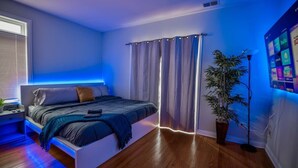 Una camera da letto moderna con un letto, tende, una pianta in vaso e uno schermo a parete che mostra icone di app.