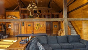 Een ruime lodge met een hoge plafond, houten wanden, een eethoek met tafel en stoelen, en een trap naar een hoger niveau.