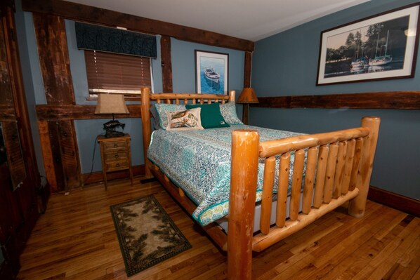 A wooden-framed bed with patterned bedding, a nightstand with a lamp, and a framed picture on the wall.