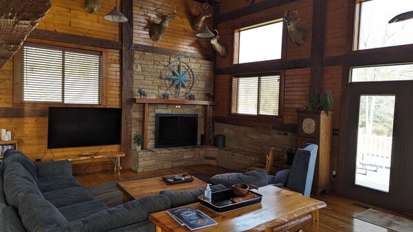 A rustic cabin interior with a stone fireplace, wooden walls, and a large window.