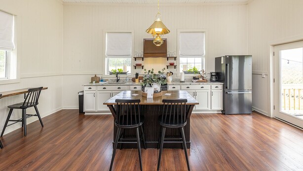 A spacious kitchen with a central island, white cabinetry, a stainless steel refrigerator, and a hanging pendant light. - The Little Red Schoolhouse (Cross Junction)