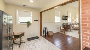 A room with a wooden floor, a mirror, a wooden desk, a chair, a small stool, and a plant. - The Little Red Schoolhouse (Cross Junction)
