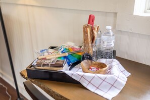 Una bandeja con bocadillos, una barra de chocolate, malvaviscos, un cuchillo de mango rojo, un cuenco de madera y una botella de agua.