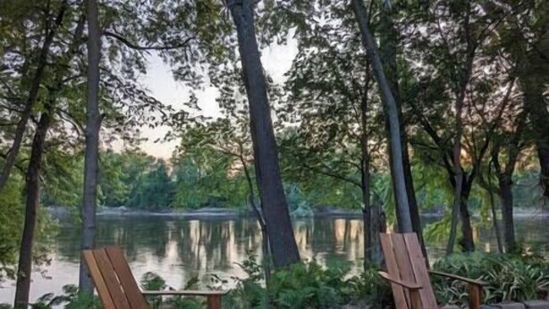 Dos sillas de madera frente a un lago tranquilo rodeado de árboles.