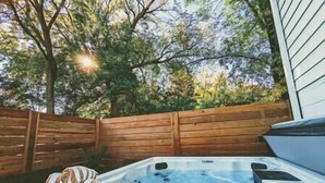Un jacuzzi en un patio trasero con una valla de madera y árboles al fondo.
