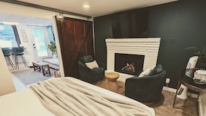 Un dormitorio moderno con una cama grande, una chimenea, dos sillones y una mesita.