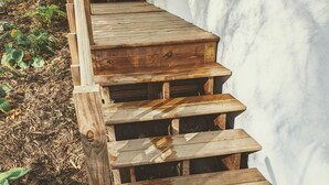 A wooden staircase with a brick base, surrounded by mulch and plants. - Hidden Garden Suite & Spa (Minneapolis)