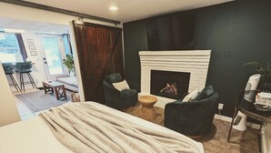 A modern bedroom with a large bed, a fireplace, two armchairs, and a small table. - Hidden Garden Suite & Spa (Minneapolis)