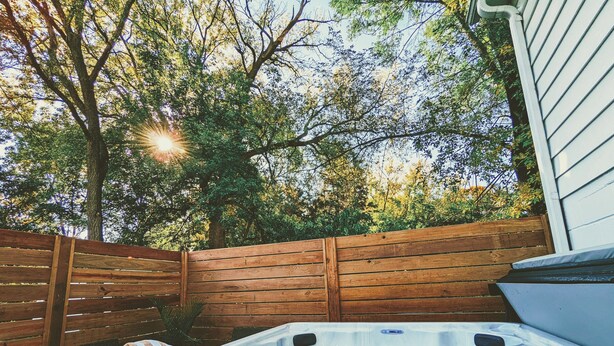 A hot tub with a control panel, a wooden fence, and a bench with a striped towel. - Hidden Garden Suite & Spa (Minneapolis)
