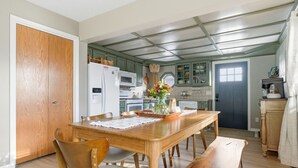 A dining area with a wooden table, chairs, and a bench. There is a kitchen in the background with green cabinets and a blue door. - Cozy Lakeside Cottage for Families and Fun Seekers. Game room - Large Soaker Tub (Council Bluffs)