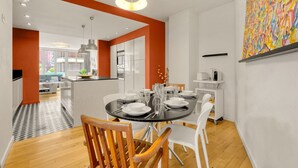 A modern dining area with a round table set for six, white chairs, and a kitchen in the background. - Le Bonrepos - T3 sur les Ramblas de Toulouse (Toulouse)
