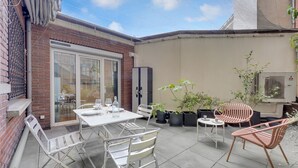 A patio area with a table and chairs, potted plants, and a sliding glass door leading to an indoor space. - Le Bonrepos - T3 sur les Ramblas de Toulouse (Toulouse)