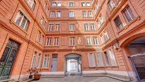 A multi-story building with a central courtyard, featuring a symmetrical facade with evenly spaced windows and a central archway. - Bleu du Maine - Elegant T3 avec terrasse (Toulouse)