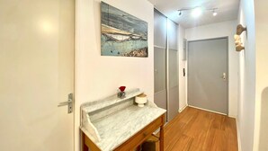 Un corridoio con un piano di lavoro in marmo, un tavolino con un vaso di fiori rossi e un quadro appeso al muro.
